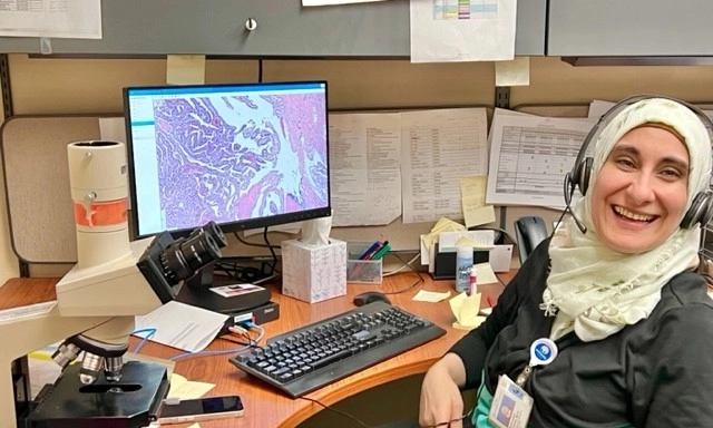 A pathology resident sits smiling in front of her computer at the hospital.