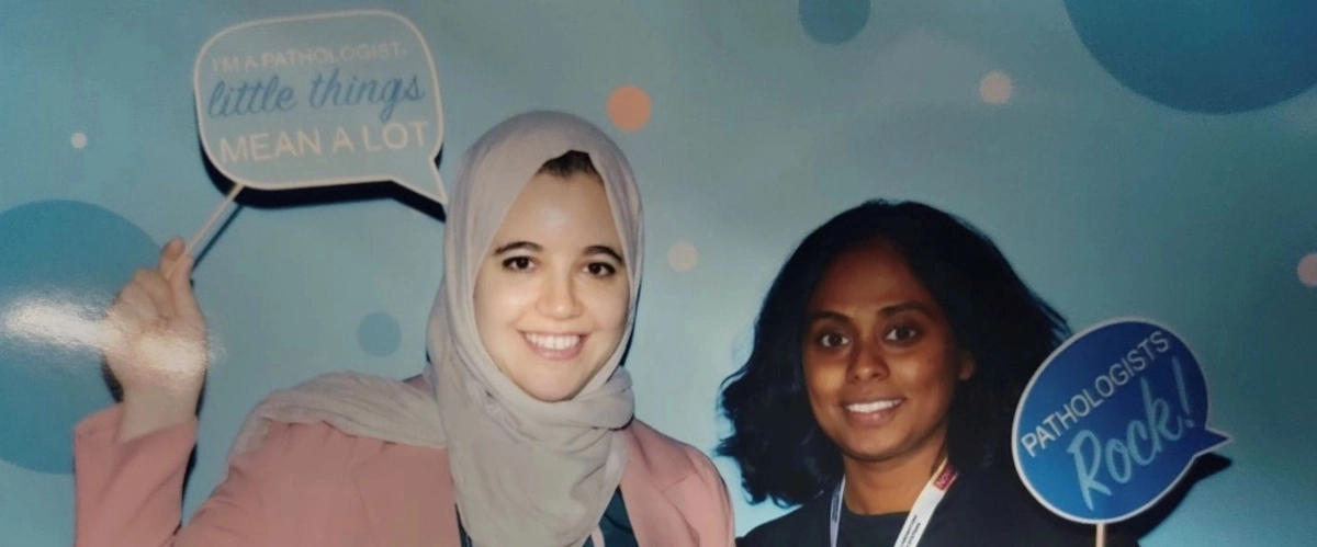 Two pathology residents smiling while holding up signs at an event.