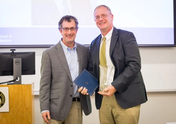 One faculty member presenting another faculty member with an award at the Faculty Award and Promotion Celebration event.