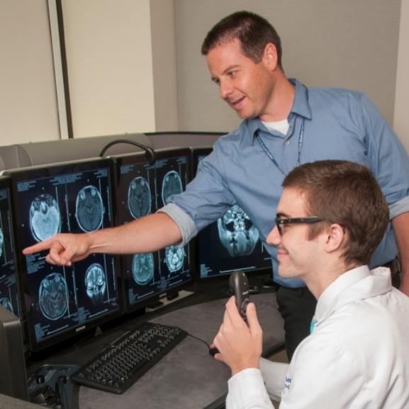 A Radiologist demonstrates a radiology machine to a student.