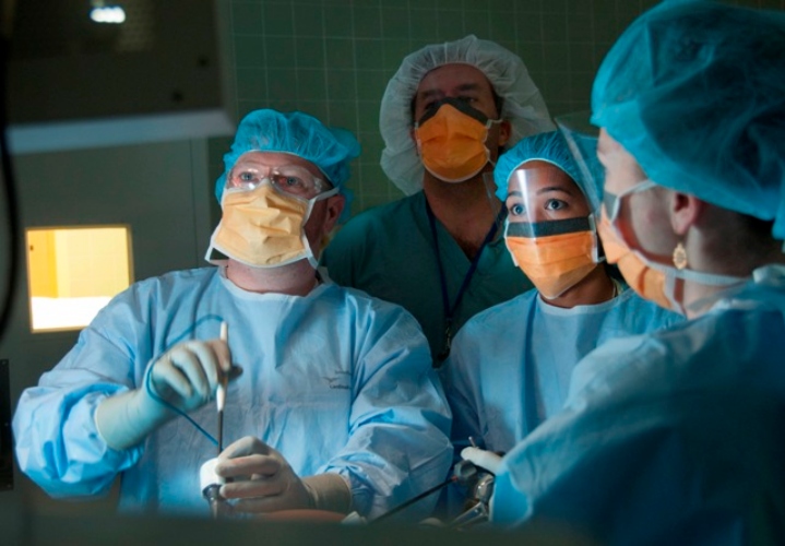 Four people wearing blue scrubs look up at a screen while performing surgery