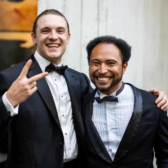 Two School of Medicine alumni smiling and posing for fun photo in their suits and ties at a formal event.