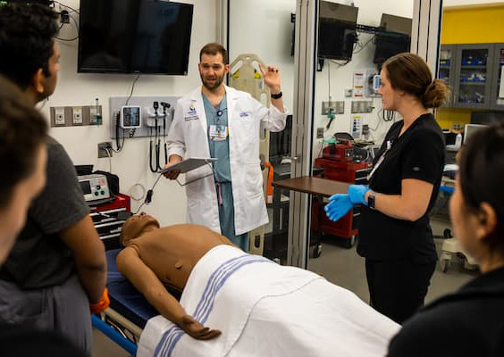 M.D. students listen while a faculty member provides instruction in the simulation lab.