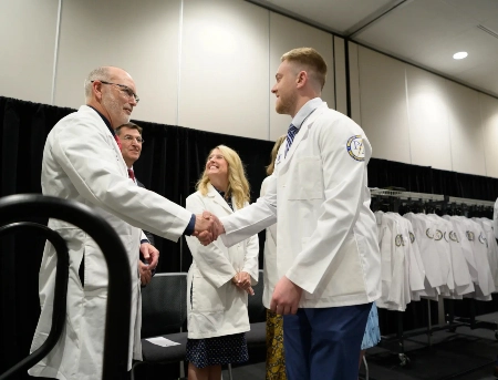 Physician Assistant student shakes hand of faculty member during graduation