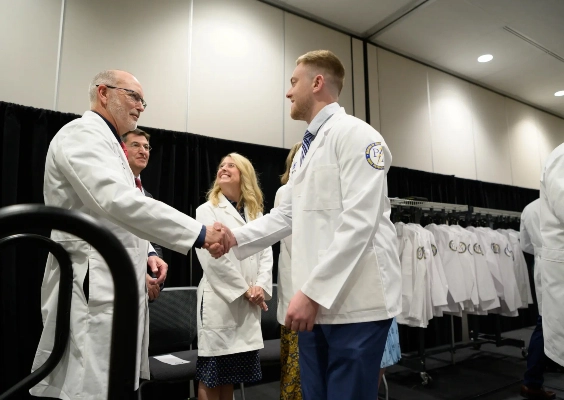 A medical student and faculty member shake hands at the Physician Assistant White Coat Ceremony.