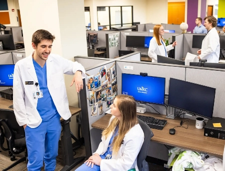 Person standing up at desk talking to person sitting down